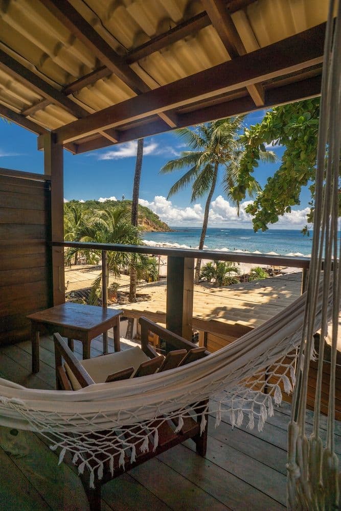 Wooden veranda with a hammock, table and chairs overlooking palm trees and the sea